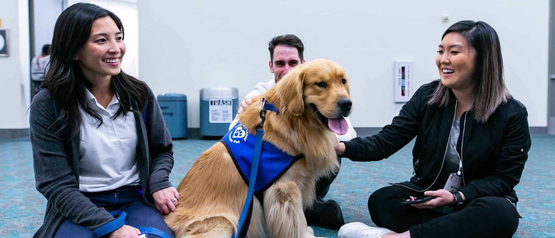 Two women and one man sit around a golden retriever service dog.
