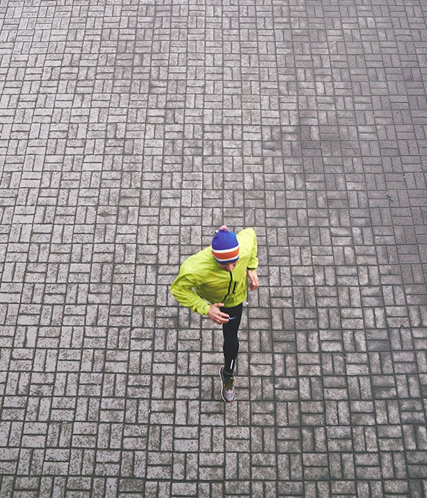 A man in a green jacket running on a concrete path