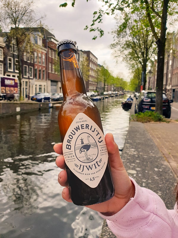 Someone holding a local Amsterdam beer in their hand with the canals in background
