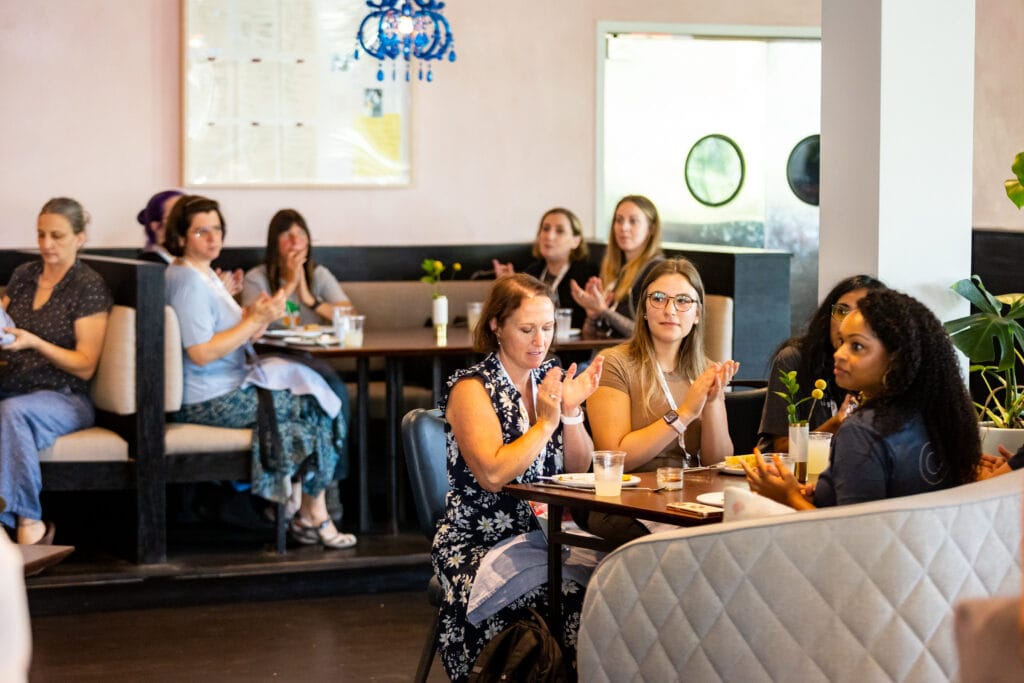 A restaurant full of women and non-binary people, eating a meal and talking to each other.