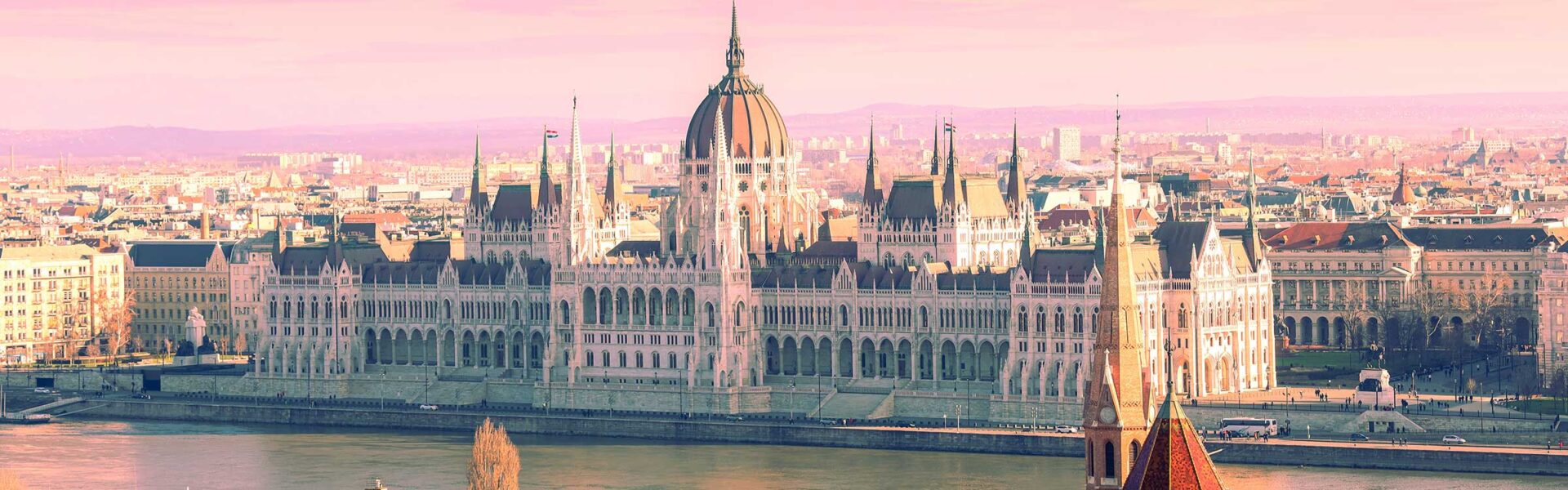 The Budapest Parliament building on the edge of the river at sunset.