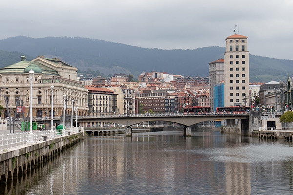 A river in Bilbao surrounded by buildings with mountains in the background.