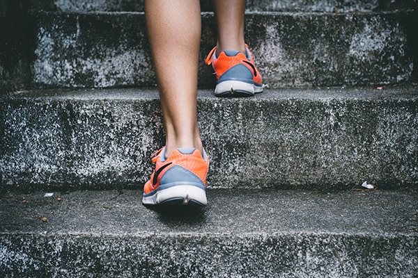 Close up of a person walking up concrete steps with running shoes on.
