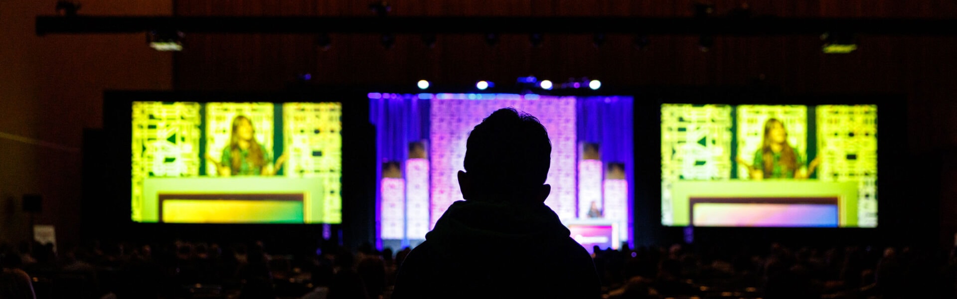 The silhouette of the back of an attendee listening to a keynote speaker.