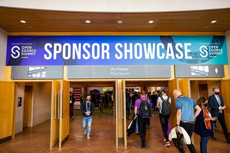 Event attendees walking through through doors. The doors have a large sign over them that says "Open Source Summit Europe Sponsor Showcase."