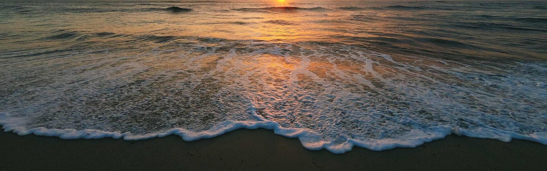Ocean waves rolling onto a beach at sunset.