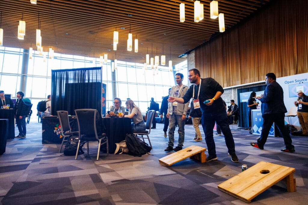 Two men play cornhole in the Solutions Showcase, while other people mingle in the background.