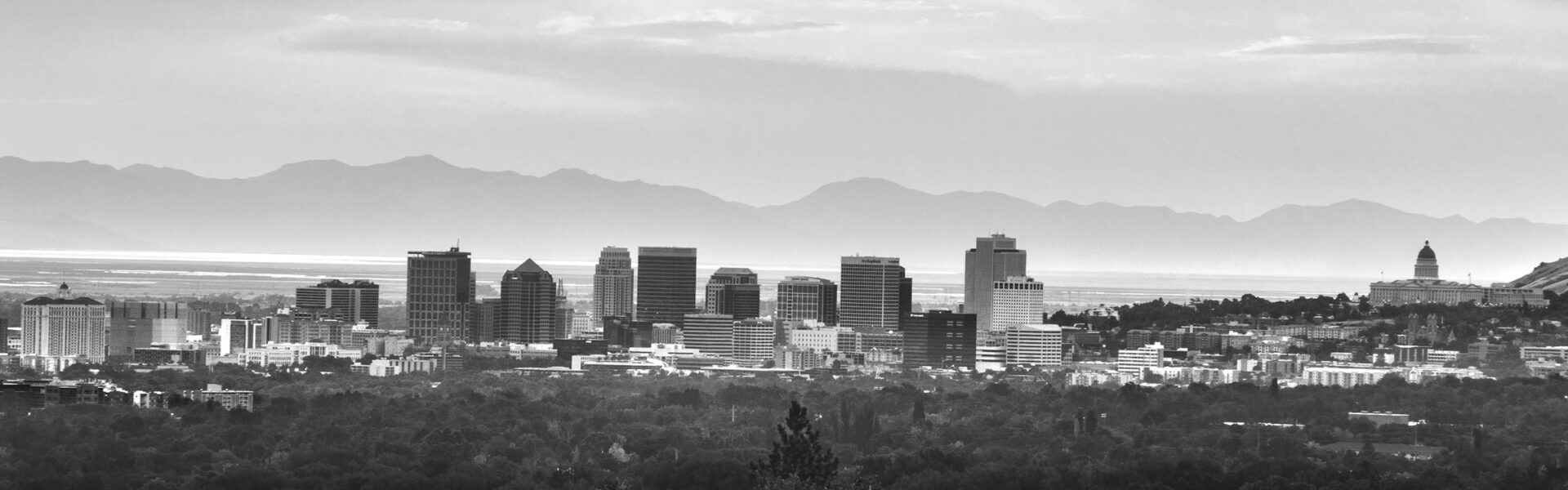Black and white photograph of Salt Lake City, Utah with mountains and clouds behind it.