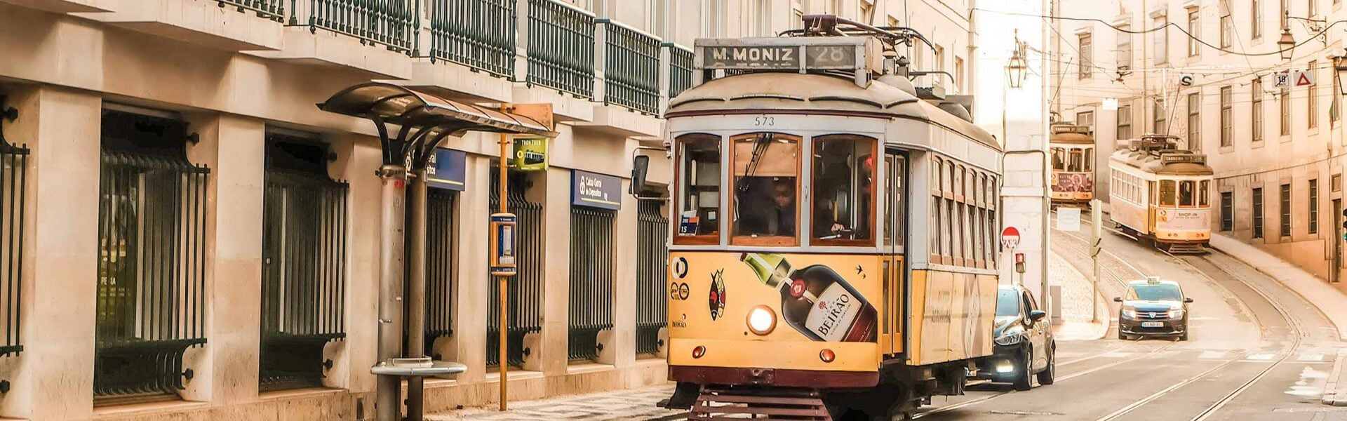 Yellow trams on a street in Lisbon, Portugal with tall beige buildings on either side.