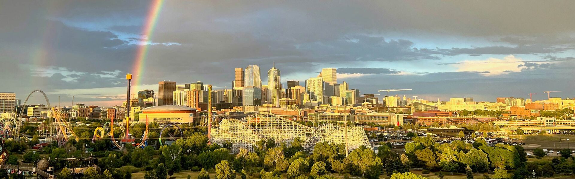 The skyline of Denver with an amusement park in the foreground and a double rainbow above.
