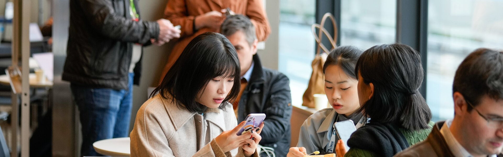 Three women seated at a table looking up information on their phones.