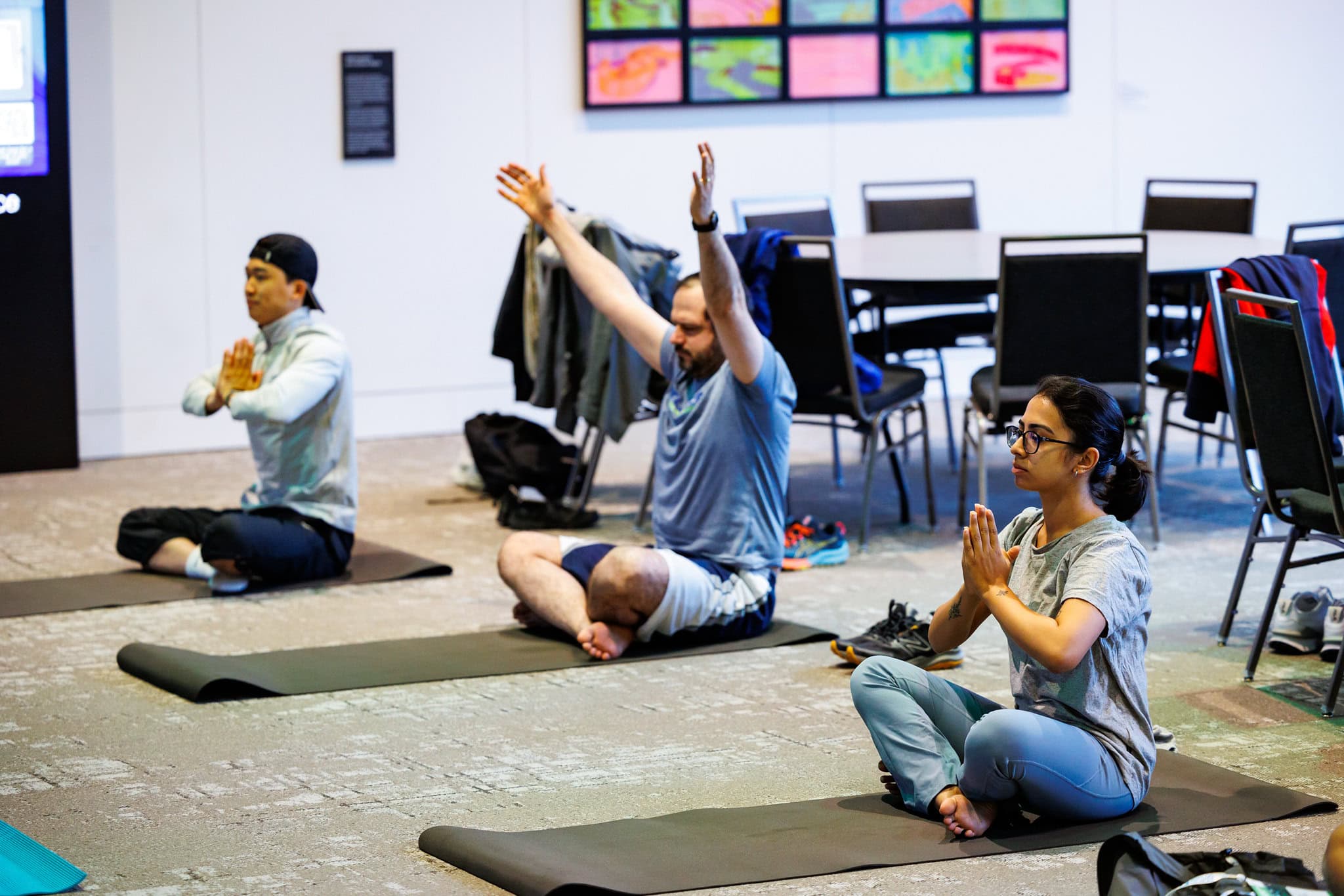 Three people sit on yoga mats doing yoga poses.