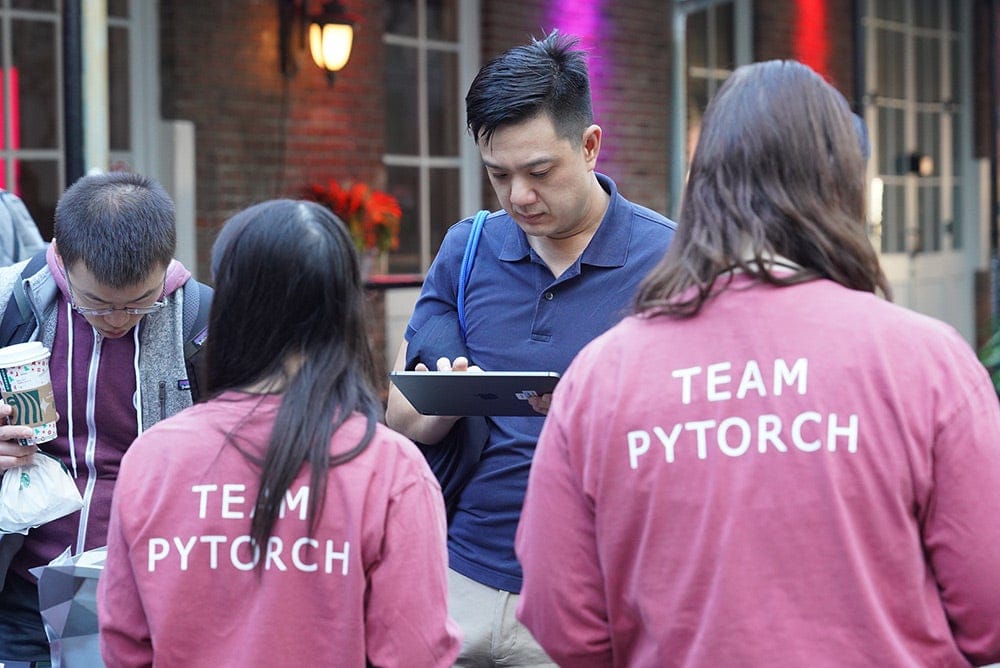 Two people with shirts that read "Team PyTorch" assisting attendees.
