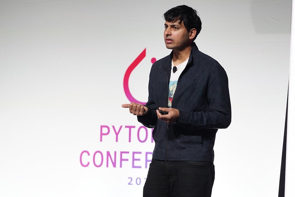A man speaking on stage with the PyTorch logo behind him.