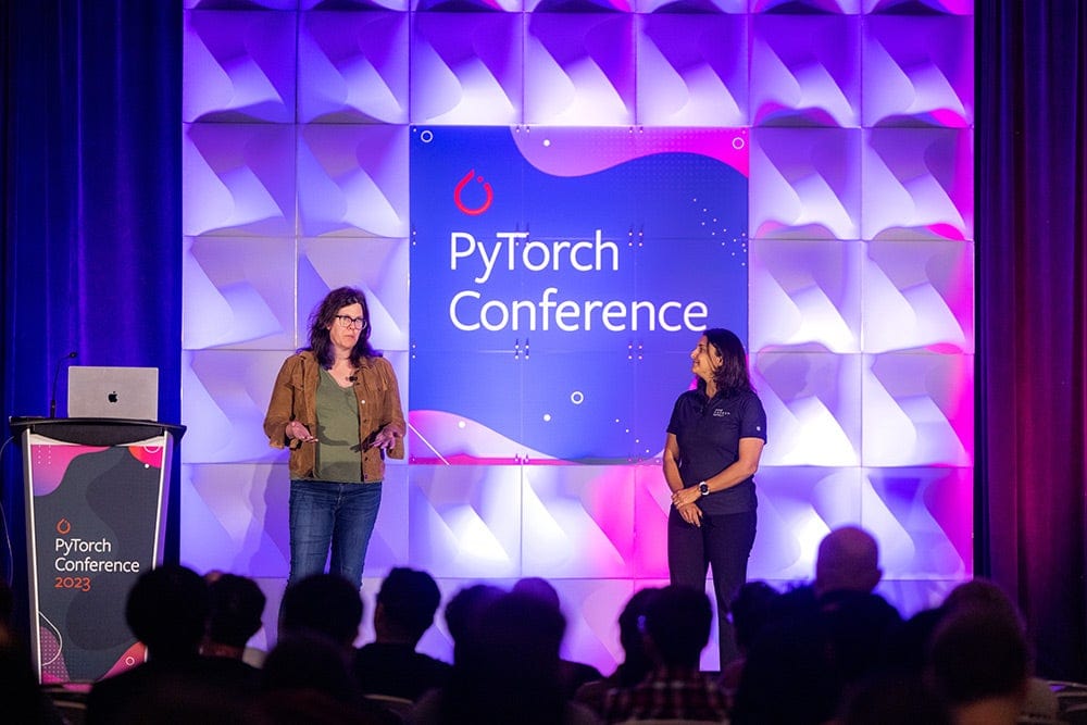 Two women speaking on stage with a sign behind them that says PyTorch Conference.