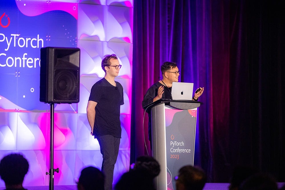 Two men speaking on stage with a sign behind them that says PyTorch Conference.