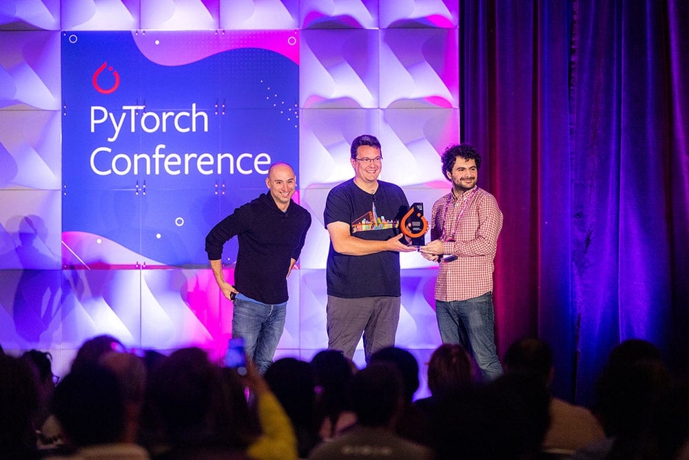Three people on a stage holding a PyTorch award.