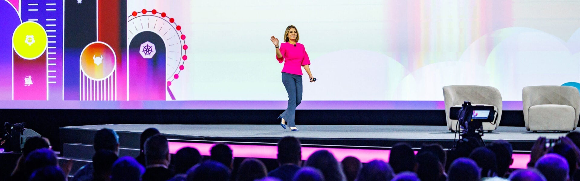 A woman walking onto a stage, smiling and waving at the crowd.