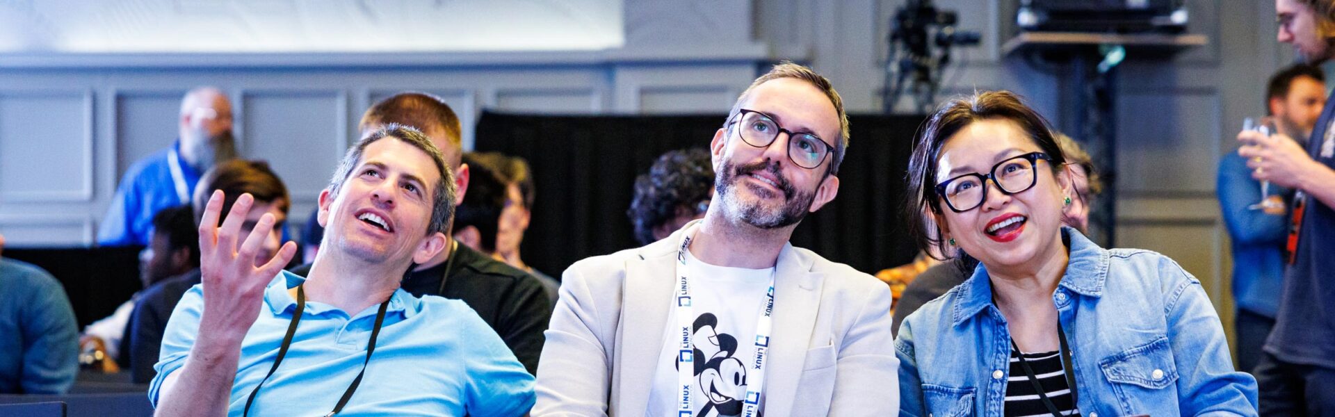 A close up of 3 attendees in the crowd smiling and engaged in the presentation.