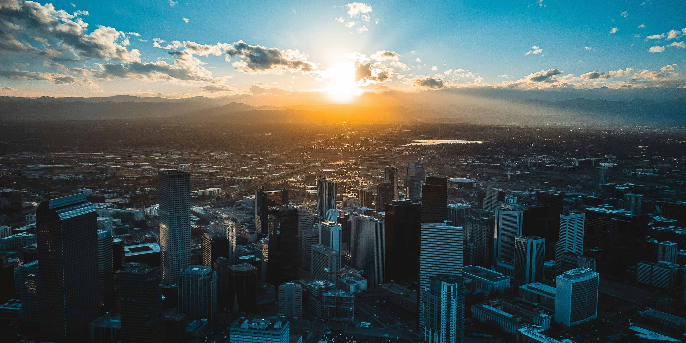 An aerial view of Denver, with the sun setting over the mountains behind it.