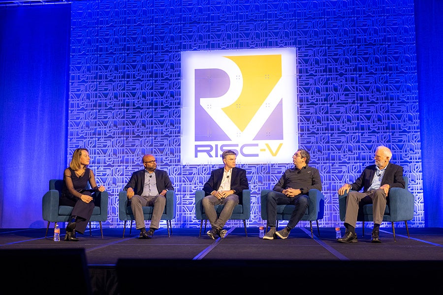 A panel of 5 speakers on stage with a sign behind them that says RISC-V