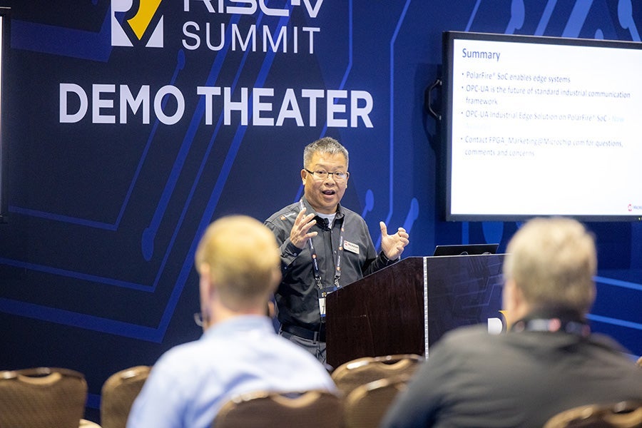 A man standing at a podium addressing the crowd with a sign behind him that says "RISC-V Summit Demo Theater"