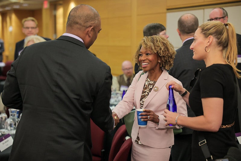 Two attendees shaking hands, with other attendees gathered around them.