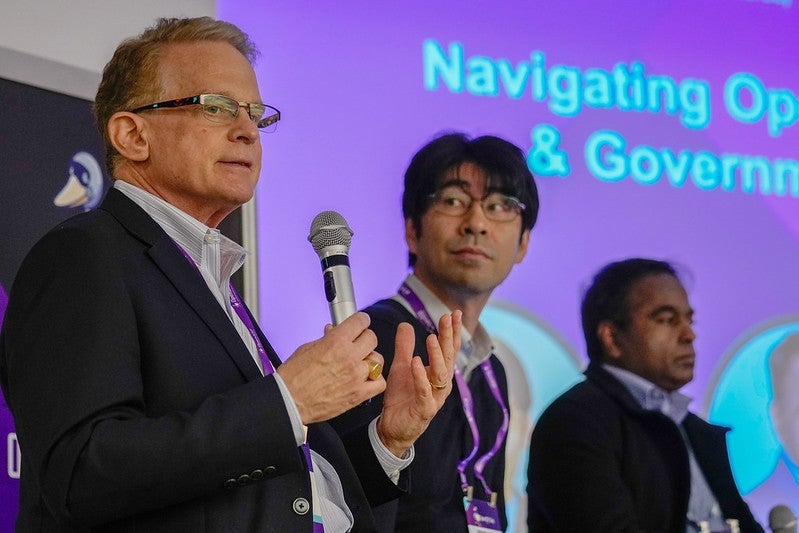 three men standing in a row on stage, one is holding a microphone.