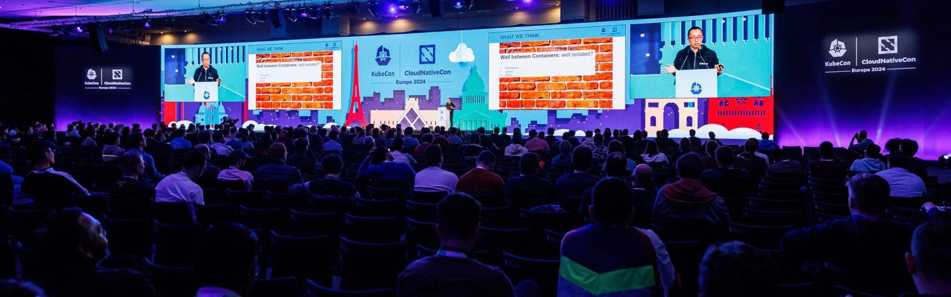 A large seated crowd with a bright and colorful stage at the front of the room.