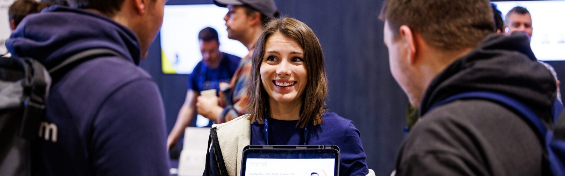 A woman holding up a tablet and smiling, two other attendees are looking at the tablet.