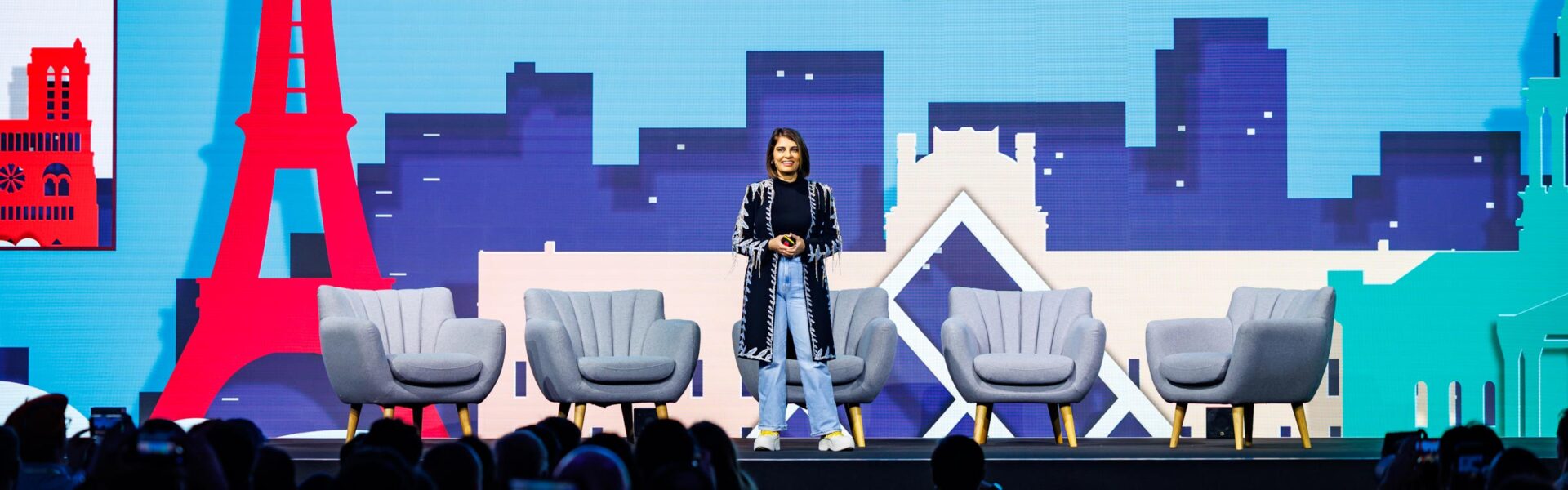 A woman standing on a colorful stage smiling at the crowd.