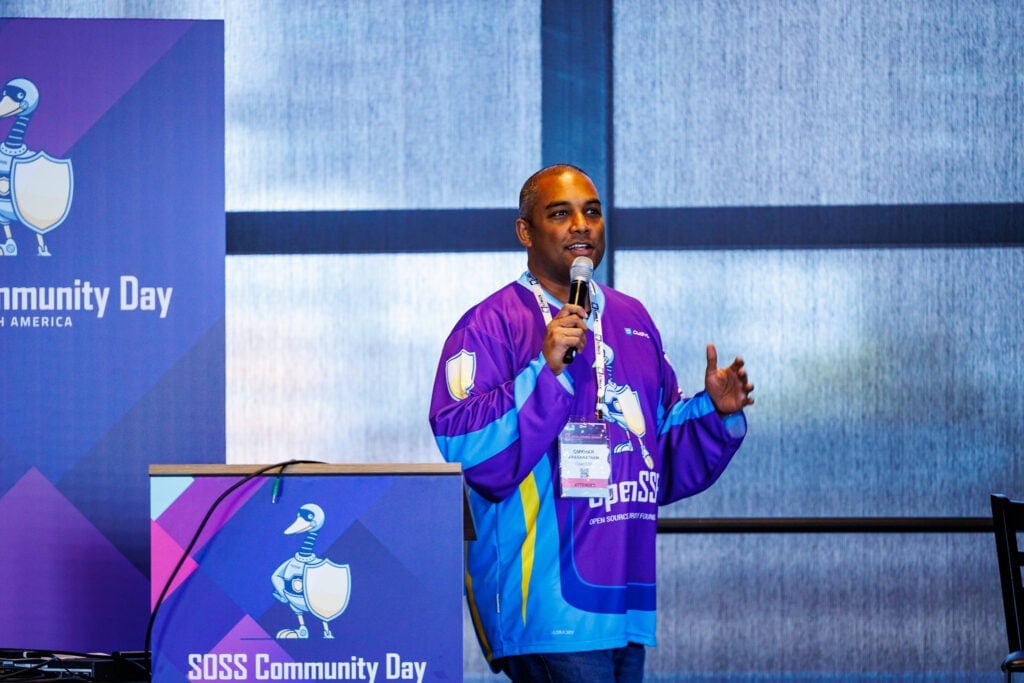 A man addressing the crowd with a microphone, wearing an OpenSSF jersey.