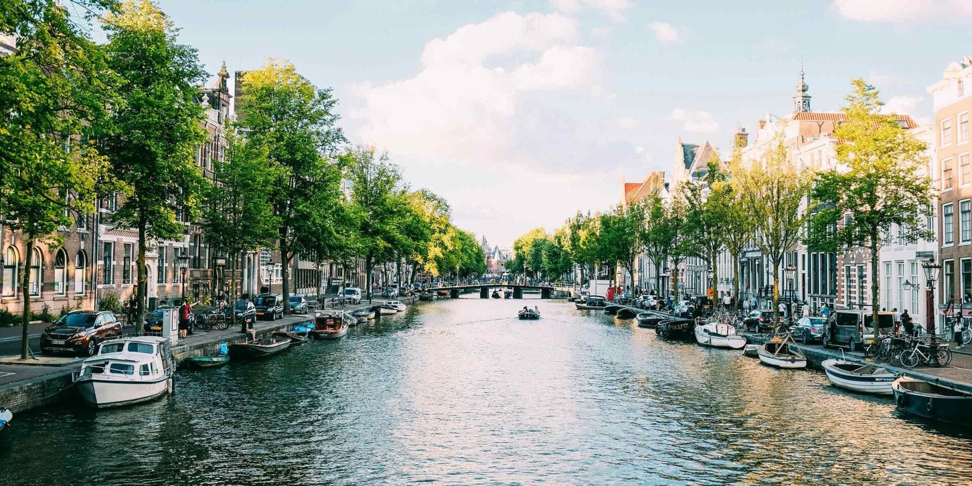 A waterway running through Amsterdam with boats along the edges of the water and buildings on either side.