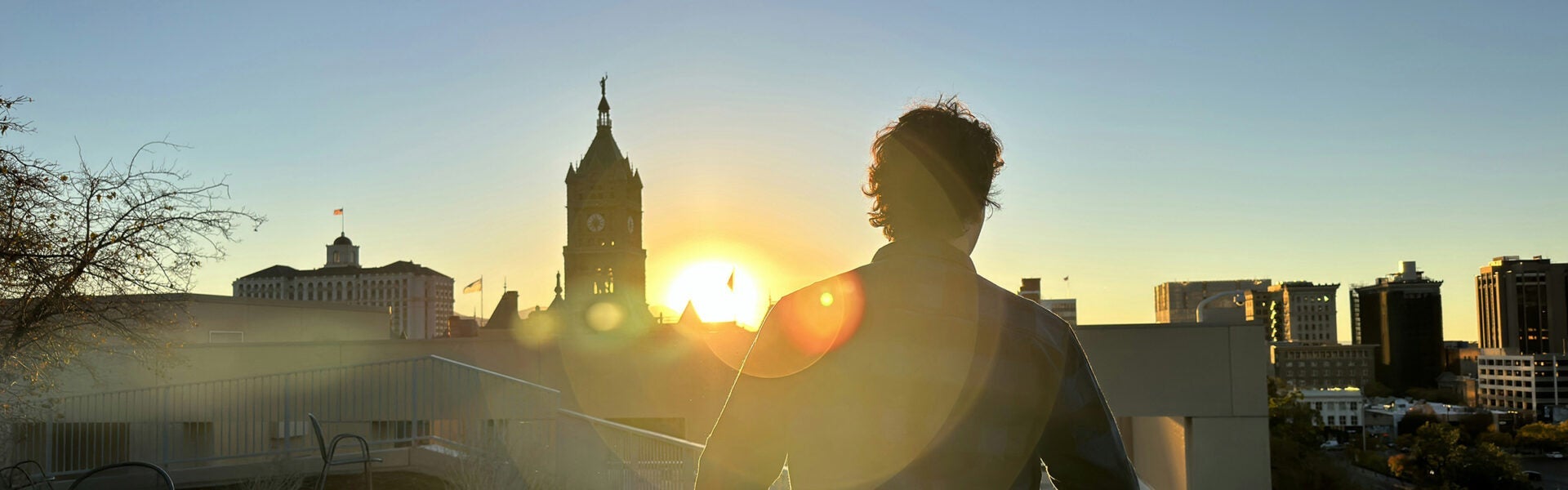 The sun setting behind the buildings of Salt Lake City & a man walking towards it.