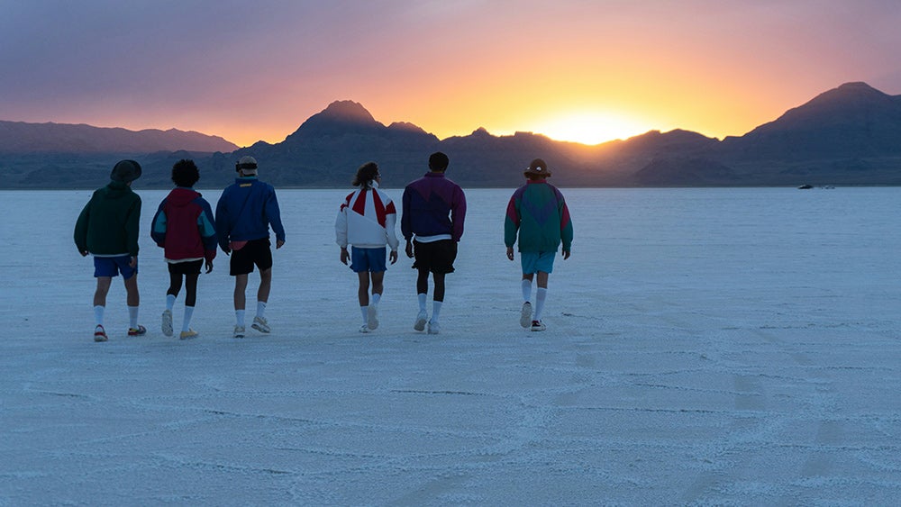 Six people in shorts and jackets walking towards the mountains on Bonneville Salt Flats in Utah.