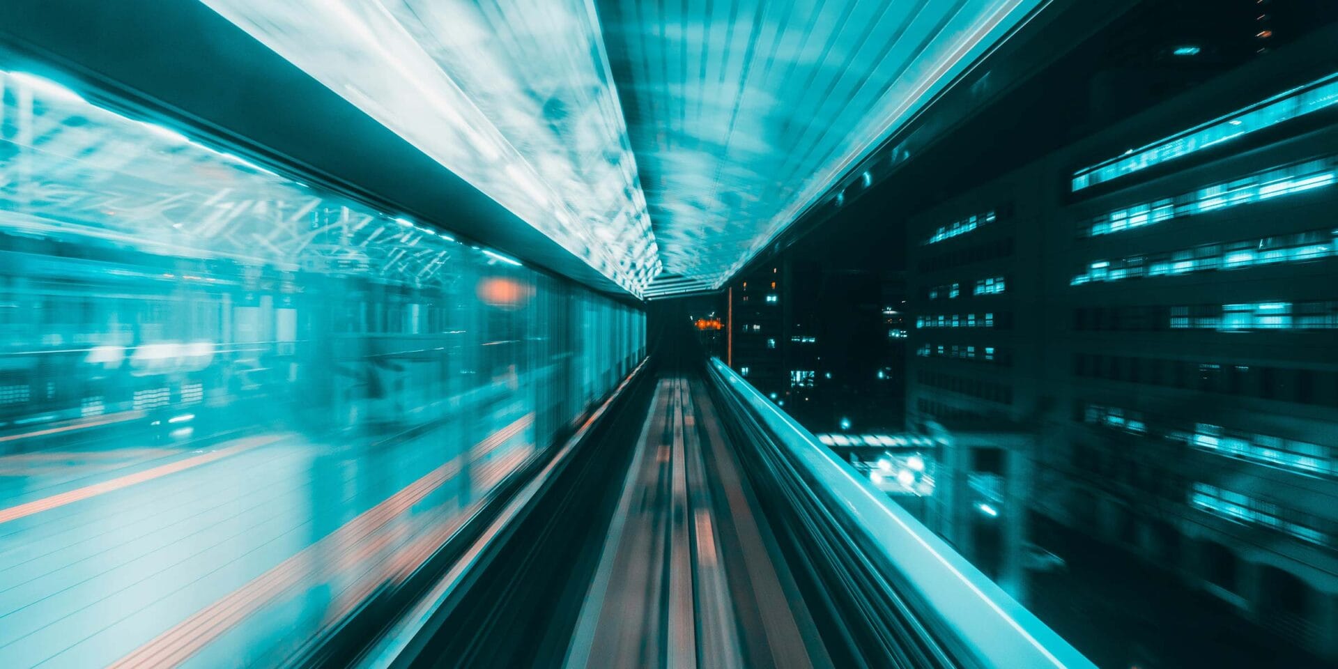 A train moving by quickly at night with the tracks lit with a light blue light.