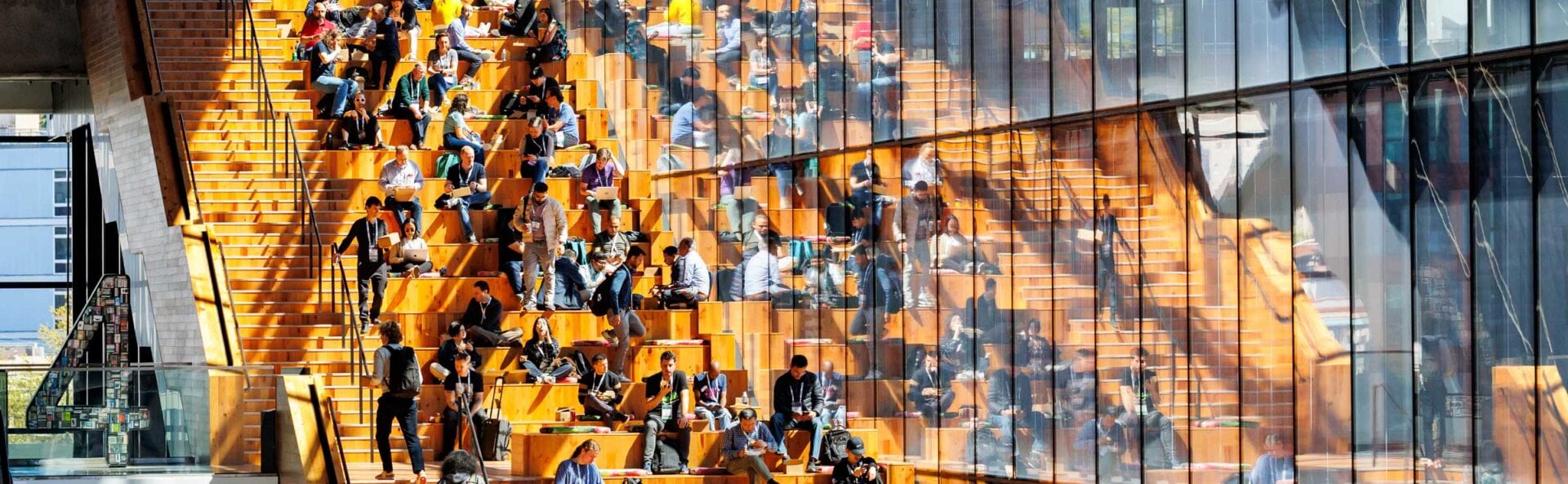 Event attendees lounging on wide stairs near a large reflective window.