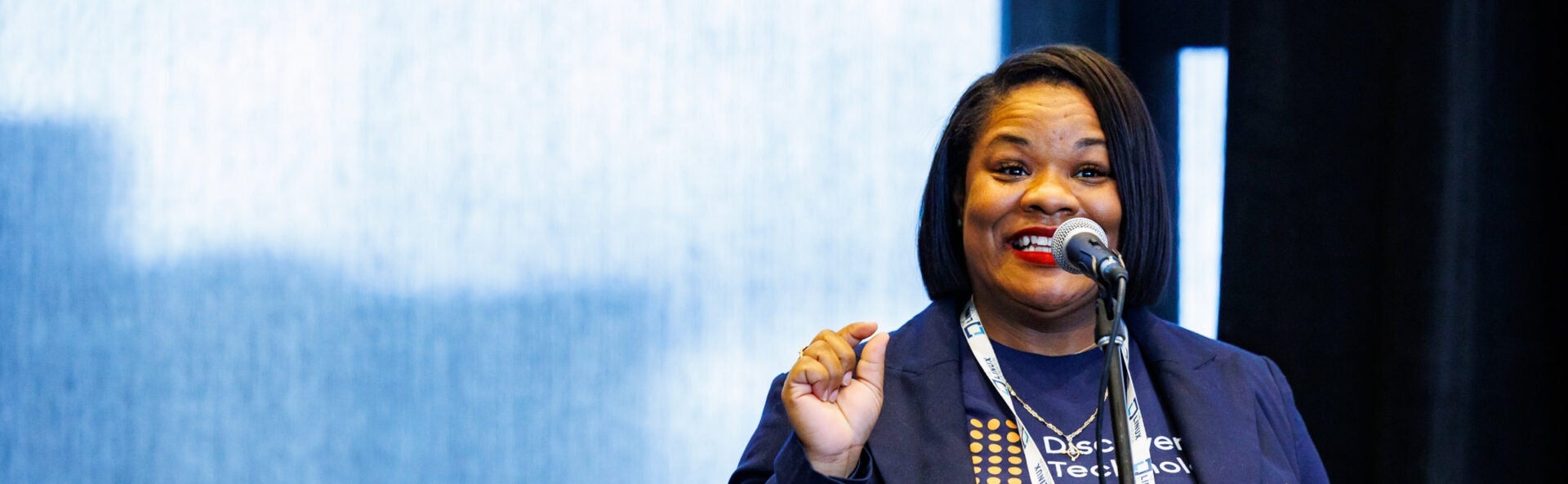 A woman smiling and speaking into a microphone.