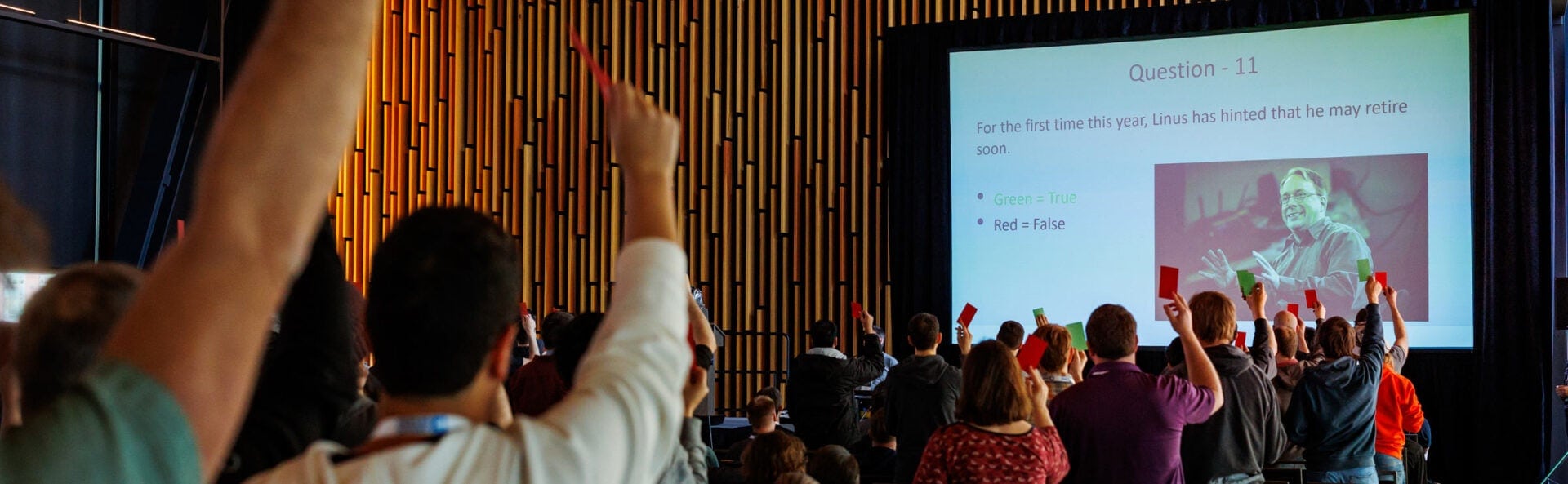 A crowd of attendees raising red or green cards after being prompted by a question on the monitor.