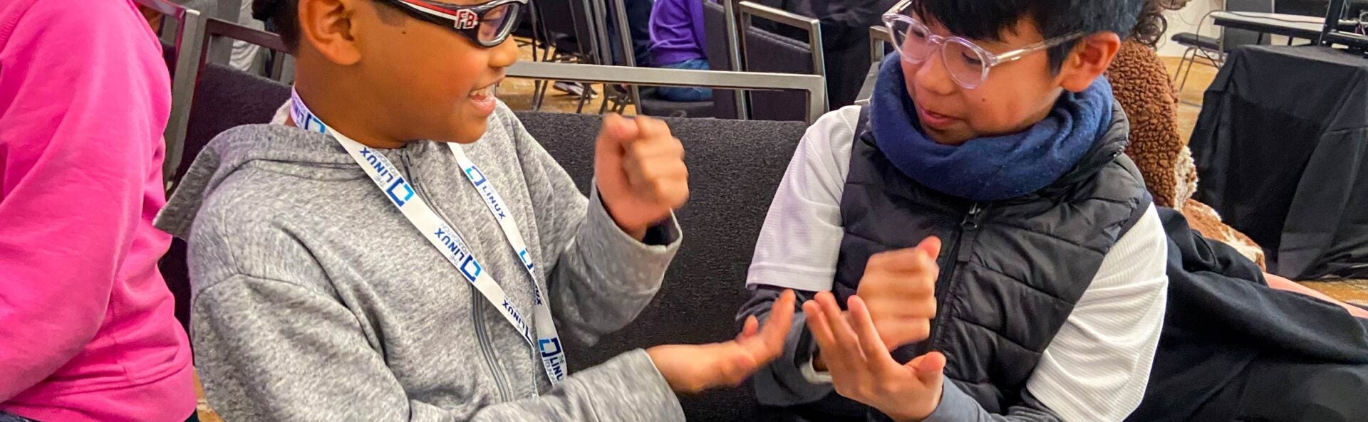 Two young children wearing glasses and an event badge smiling and playing rock, paper, scissors.