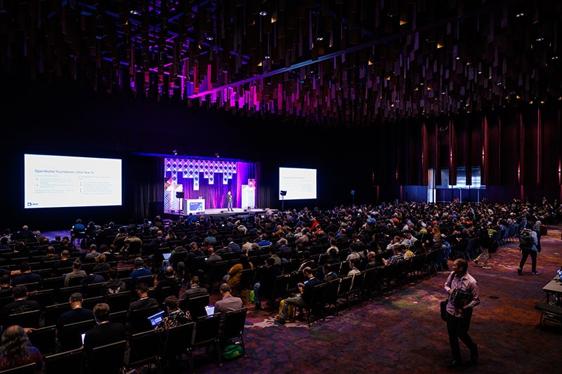 A large crowd seated and listening to a keynote speaker.