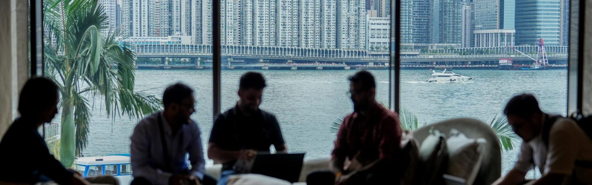 A group of attendees seated in front of a large window showing a boat on the water and the city in the background.