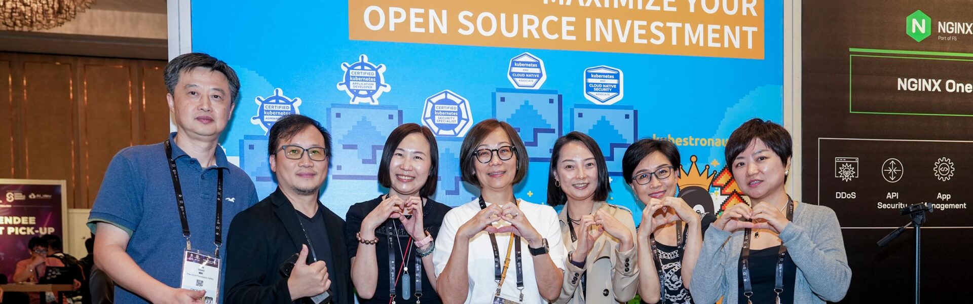 Seven attendees in a group photo. The women are holding up heart hands and the men are giving a thumbs up.