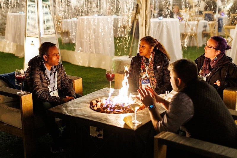 Four people around a fire drinking wine and talking.