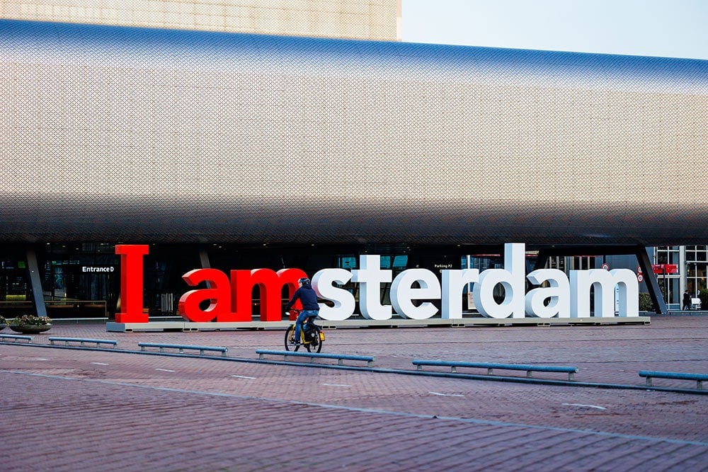 A sign that says "I amsterdam" with a person riding a bike in front of it.