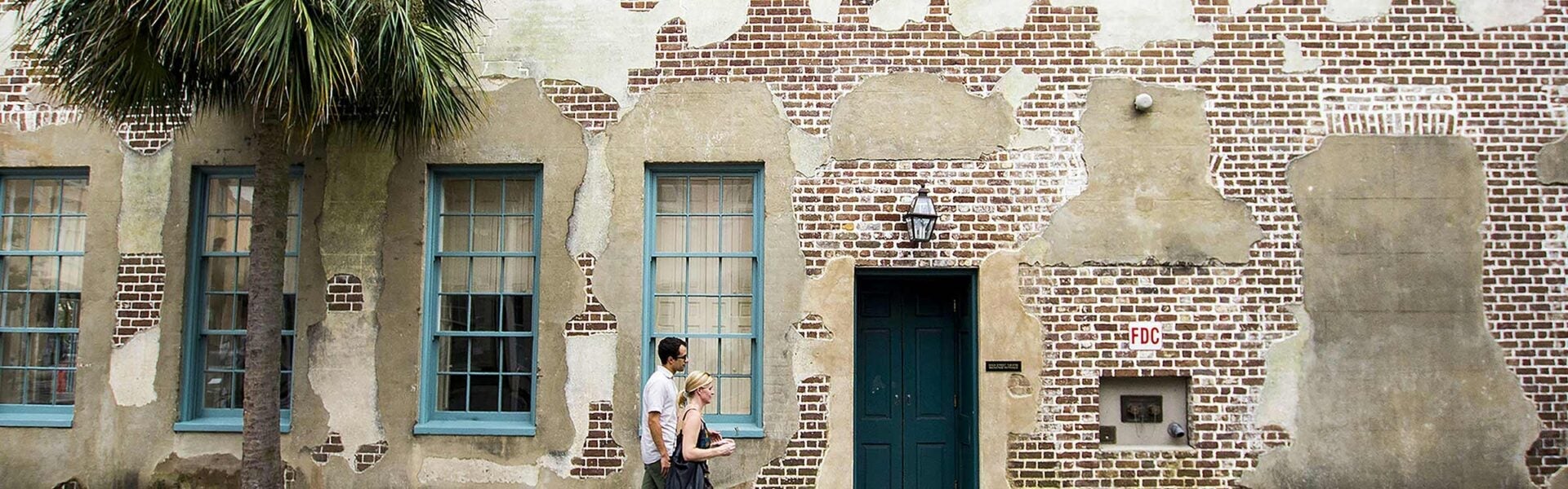 A man and a woman walking down the sidewalk in front of an old brick building.