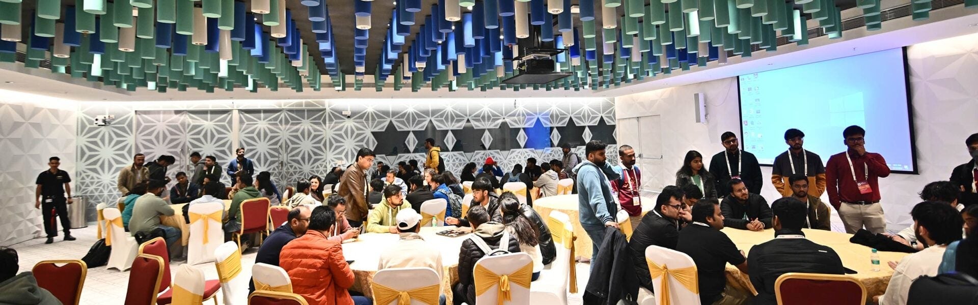 Attendees seated around round tables in a colorful room.