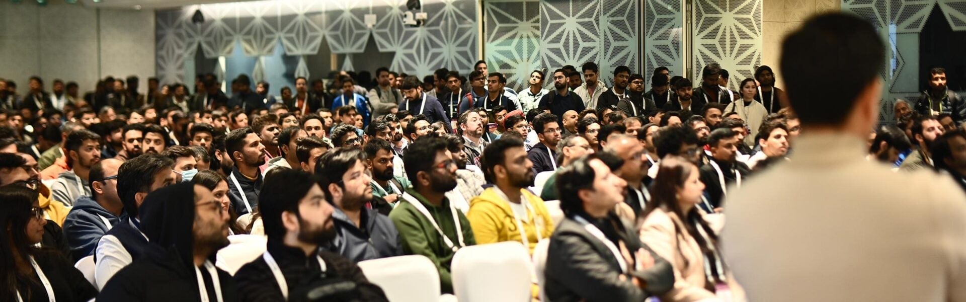 Attendees seated in a large conference room with a decorative wall behind them.