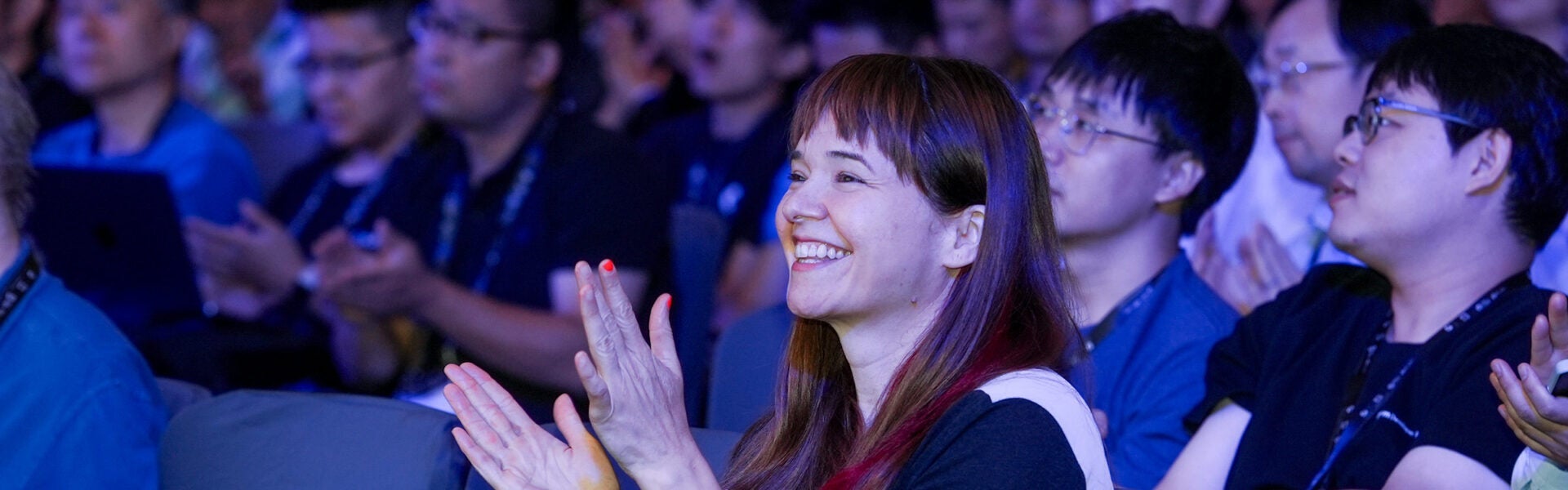 A close of up of attendees in a crowd smiling and clapping.