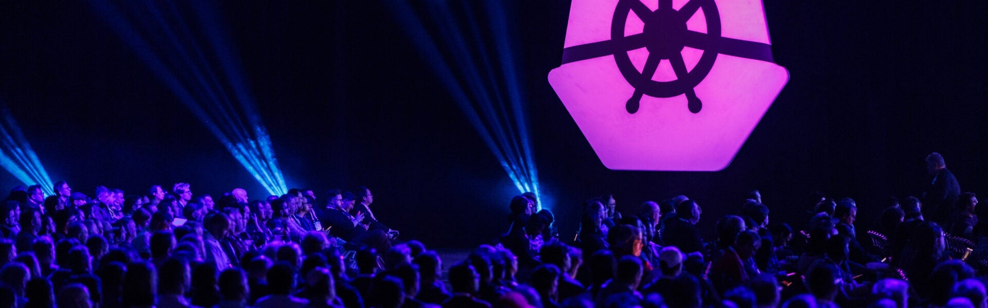 The KubeCon icon illuminated on a dark wall.